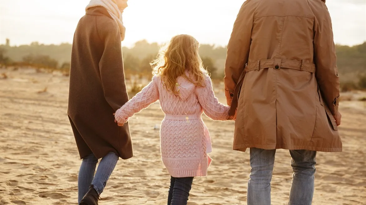 Familj i motljus, kvinna och man som håller en dotter mellan sig.