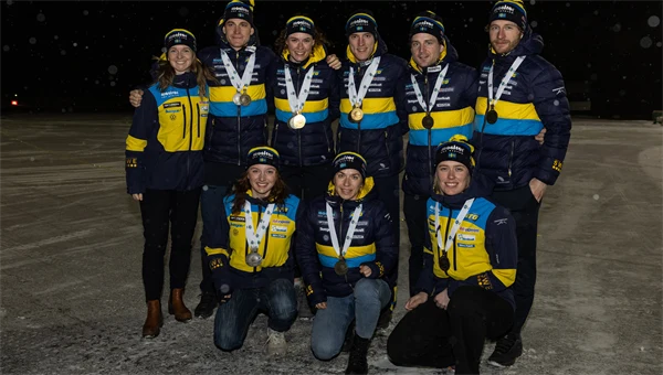 Svenska herr- och damlandslaget i skidskytte står med sina medaljer kring halsen i mörkret på Åre-Östersund Airport.