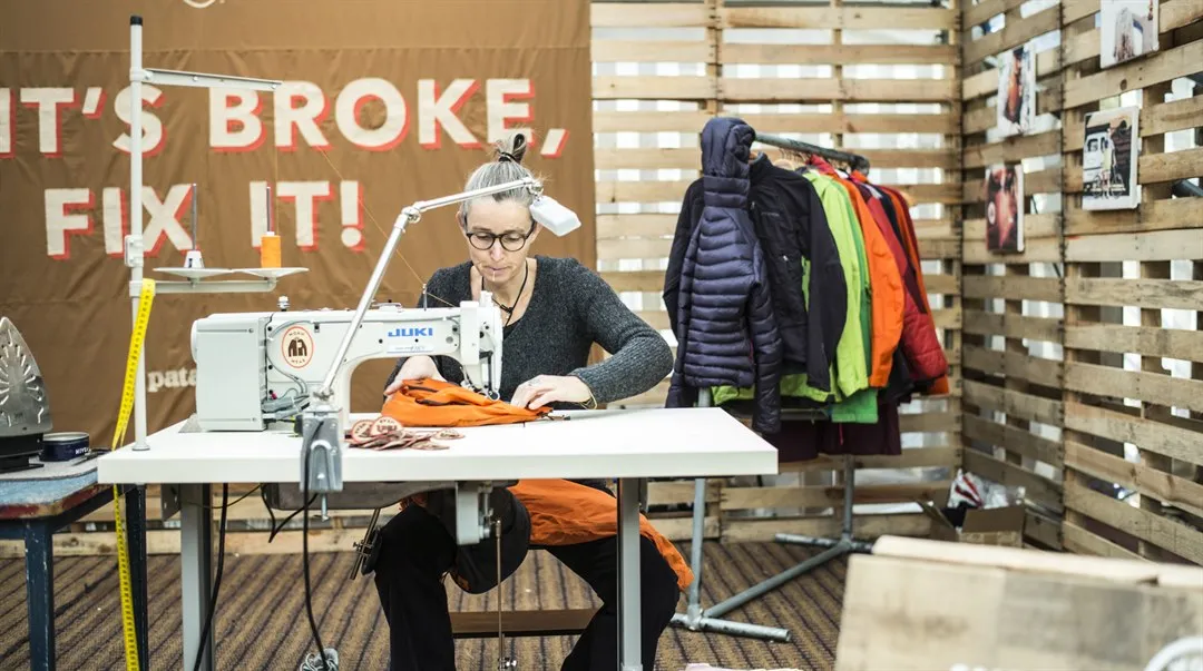 Kvinna sitter vid skrivbord och syr/lagar begagnade kläder på symaskin