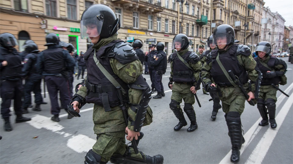 Armed soldiers in vests and helmets walk along a city street.
