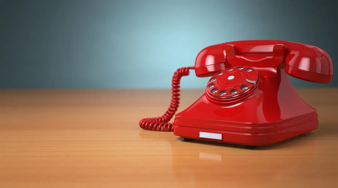 Red, vintage phone on a desk.