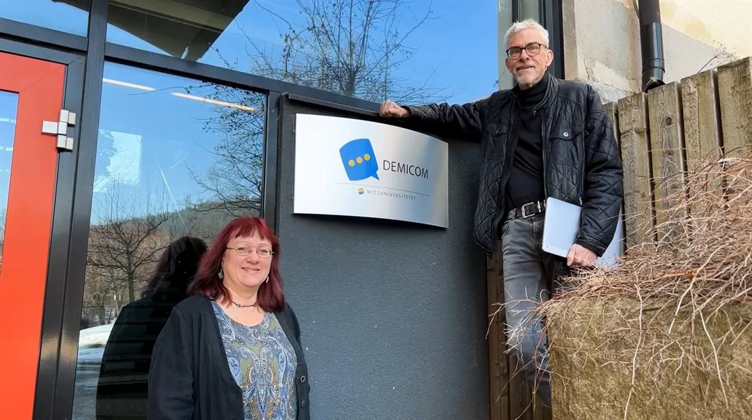 En man och en kvinna står framför en fasad med en Demicom skylt