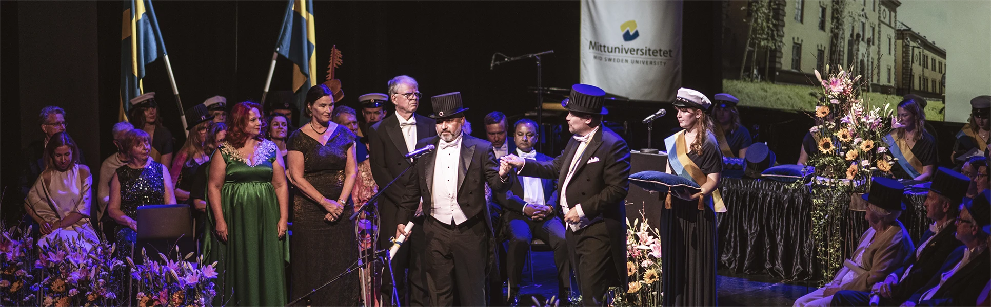 A well-dressed person with a doctor's hat is in the spotlight on a stage.