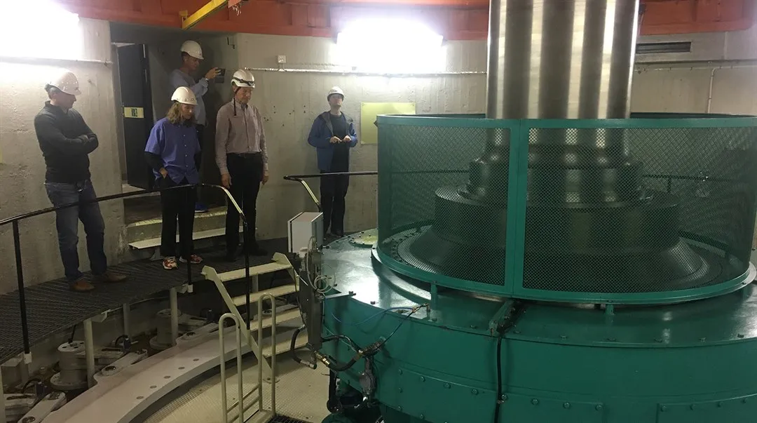 Personer står och tittar på vattenkraftverkets turbin