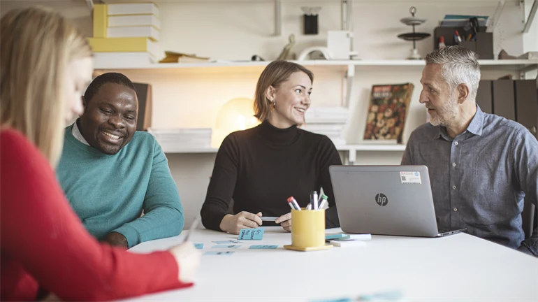 Fyra studenter runt ett bord som arbetar med en laptop och post-it lappar.